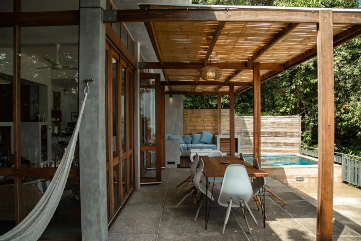 Dřevěná pergola u domu s jídelním stolem a houpací sítí