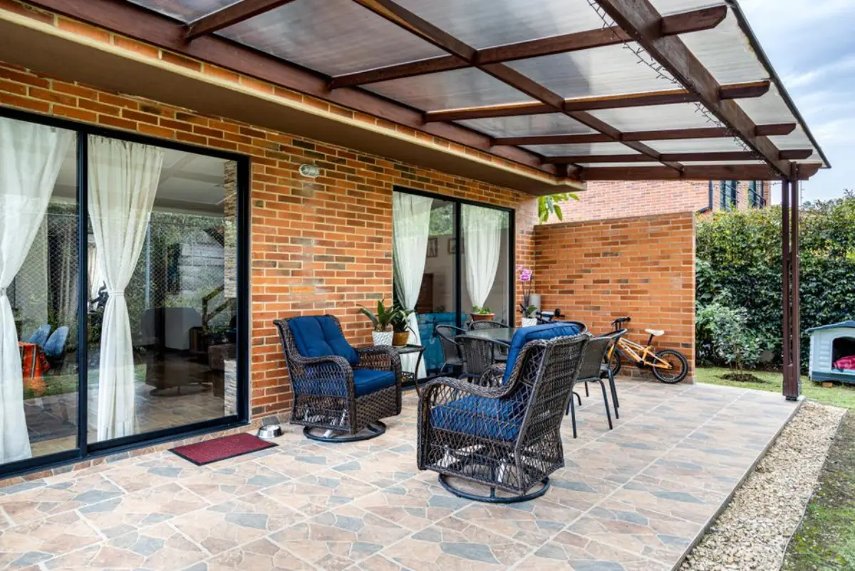 Hliníková pergola s prosklenou střechou nad terasou cihlového domu